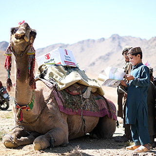 Kamele bringen Bücher zu Kindern in Afghanistan. © Save the Children Kinder stehen um ein Kamel mit Bücherkiste auf dem Rücken