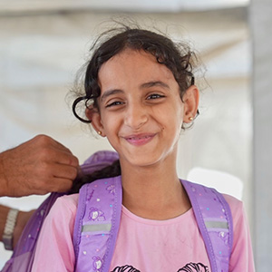 Dauerspenden helfen langfristig Kindern in Not weltweit. © Save the Children Ein lächelndes Mädchen bekommt einen Schulrucksack