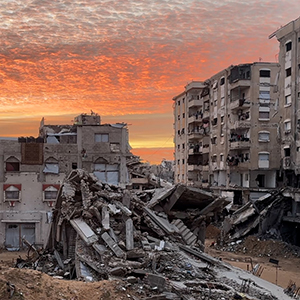 Zerstörung im Gazastreifen (Februar 2026) © Save the Children Viele zerstörte Gebäude und Trümmer säumen Wege aus Sand. Im Hintergrund geht die Sonne auf.